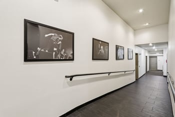 Long interior apartment hallway at Ludwig Apartments with dark tile flooring, a black handrail, a...