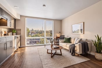 Open living room and kitchen layout with large window, staged sofa, coffee table, and wood-look flooring.