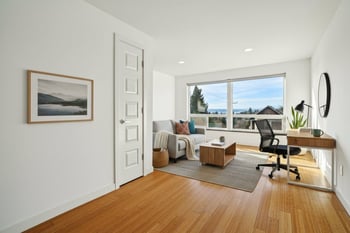 A room with a wooden floor and a large window overlooking a view of a lake and mountains.
