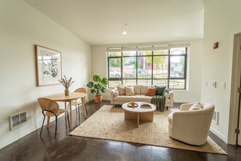 Living room with polished concrete floors, large multi-pane window, sofa, accent chair, and small dining table.