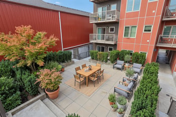 Outdoor courtyard at REV Fremont featuring a wooden dining table, lounge chairs, and potted greenery.