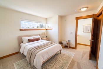 Staged bedroom at Union Bay Lofts featuring a bed, area rug, carpet flooring, wood trim, and corner clerestory windows.