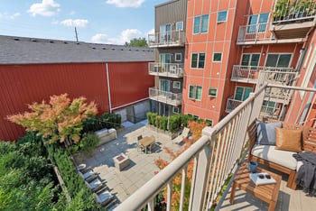 View from an upper apartment balcony looking down onto an outdoor courtyard with lounge seating, fire pit, and grill.