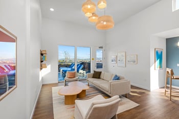 Common area lounge with sofa, armchairs, wood floor, and large windows opening to an outdoor patio.