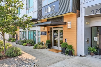 Street-level entrance of Ludwig Apartments with modern signage, awning, planters, and sidewalk landscaping.