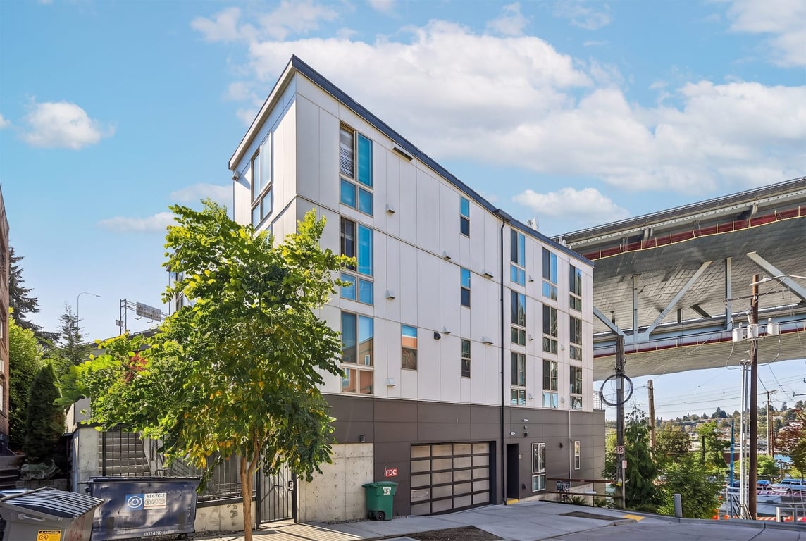 Modern multi-story apartment building exterior with white and dark gray siding and many windows.