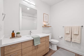 Bathroom with a wood-tone vanity, white counter, large mirror, and towel bars.