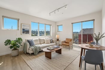 Staged living room with beige sofa, coffee table, dining area, and sliding doors opening to a balcony.
