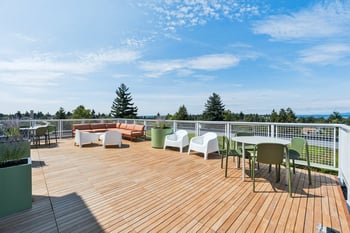 A wooden deck with white chairs and green planters.