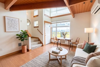 Bright loft living area with exposed wood ceiling beams, hardwood floors, dining table, and staircase.