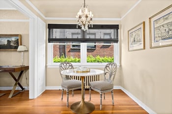 Dining nook with marble-top table, two elegant chairs, hardwood floors, and a crystal chandelier.