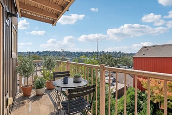 Private balcony with bistro table, chairs, and potted plants overlooking green neighborhood views.