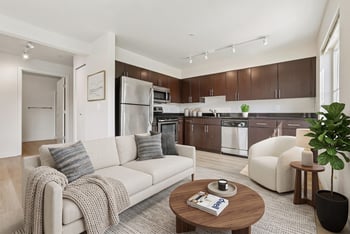 Open living room with cream sofa and coffee table next to kitchen with dark wood cabinetry and stainless appliances.