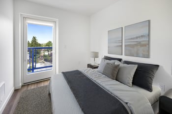 A bedroom with a large bed and a view of a blue fence and trees outside the window.