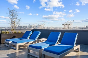 Rooftop deck with four blue lounge chairs and panoramic Seattle skyline view with port cranes