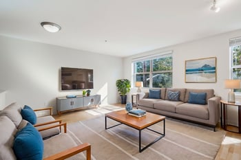 Bright living room in Gilbert House Apartments, Seattle, WA with large windows, cozy seating, and neutral decor.