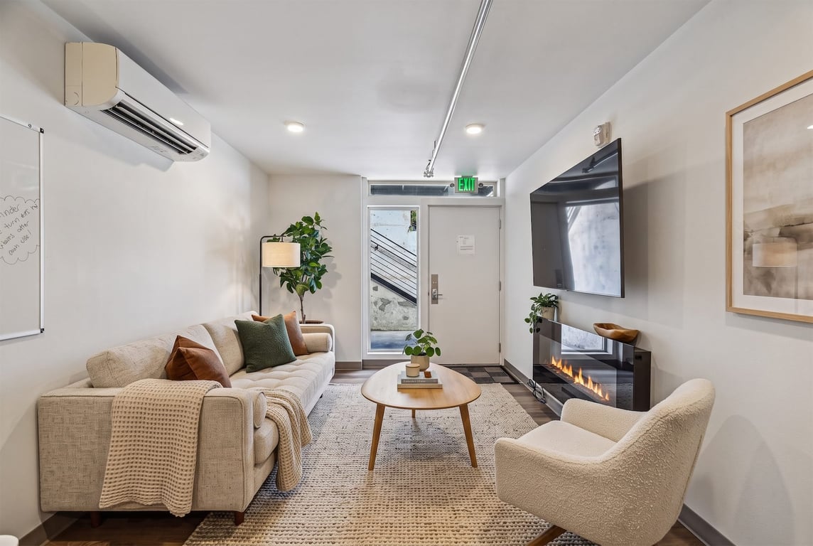 Resident lounge with sofa, accent chair, wall TV, electric fireplace, AC unit, and exterior exit.