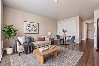Living area with beige sofa, coffee table on patterned rug, and small dining set next to closet doors.