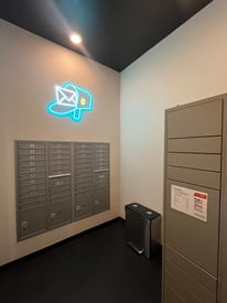 Mailroom with individual mailboxes, a large package locker system, and a neon mailbox sign.