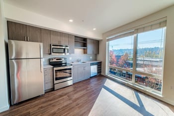 Bright living room in a Vibe Apartments unit, Seattle, with large window, hardwood floors, and modern kitchenette.