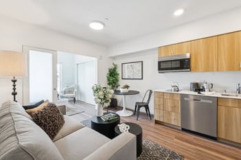 Open-concept living room, dining area, and kitchen with wood floors, light wood cabinets, and sta...