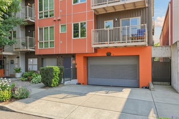 Exterior of REV Fremont showing orange and dark panel siding, upper balconies, and a secure roll-up garage entrance.