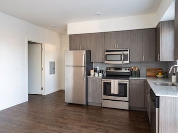 Kitchen featuring wood-grain cabinets, stainless steel appliances, speckled countertops, and dark wood-style floors.