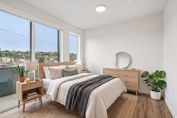 Bedroom with a queen bed, two nightstands, a dresser, and oversized windows overlooking the neighborhood.