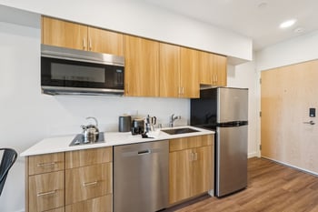 Compact kitchen with stainless steel appliances, light wood cabinets, and a two-burner stovetop.