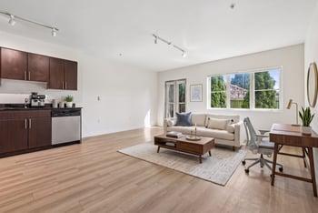 Open living area at REV Fremont with wood flooring, sofa, work desk, and corner kitchenette with dishwasher.