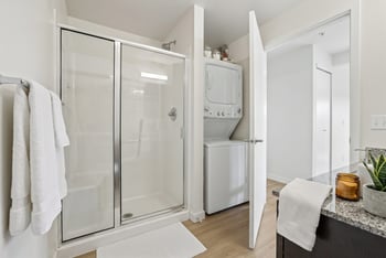 Bathroom at REV Fremont featuring a glass-door walk-in shower and stacked in-unit washer and dryer.