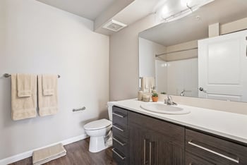 Modern bathroom featuring dark wood vanity with white countertop, large mirror, and toilet.