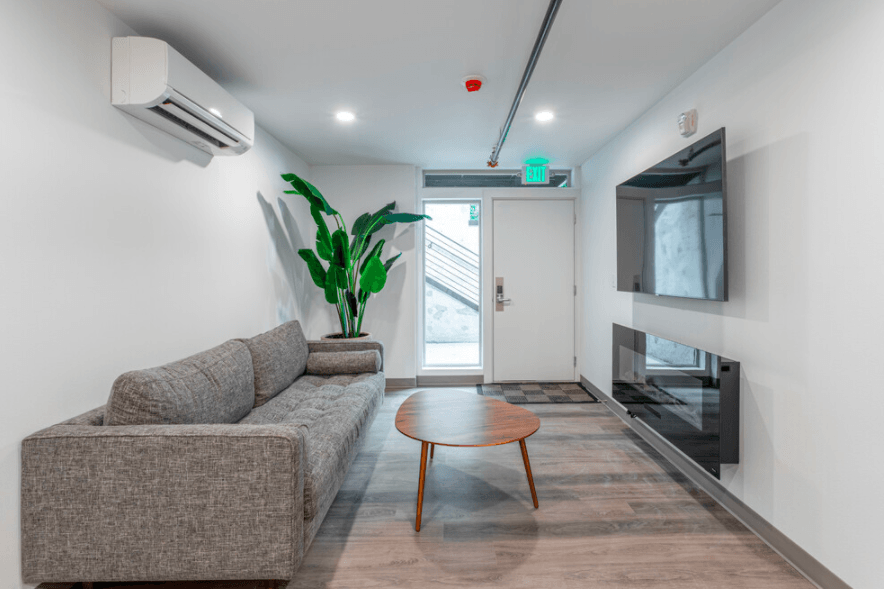 Community lounge with a gray sofa, coffee table, wall-mounted TV, and electric fireplace.