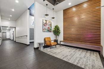 Modern residential lobby at Ludwig Apartments with a wood slat accent wall, leather armchair, and hallway.
