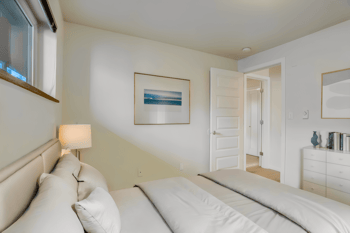 Bright bedroom with a bed, window, and door to another room.