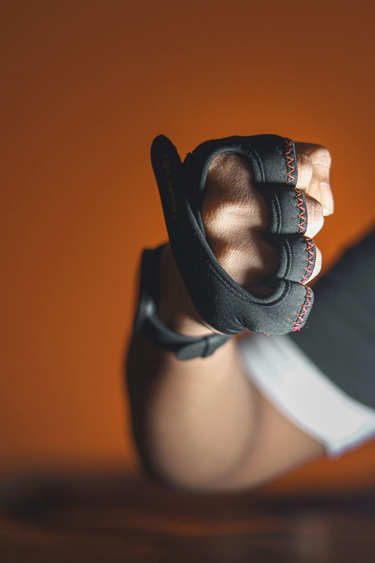Mano con guante de entrenamiento negro sobre fondo naranja