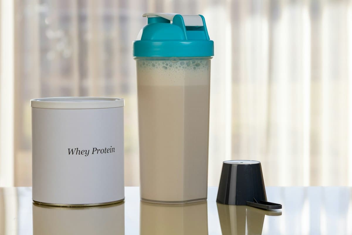 Shaker con batido junto a un envase de proteína