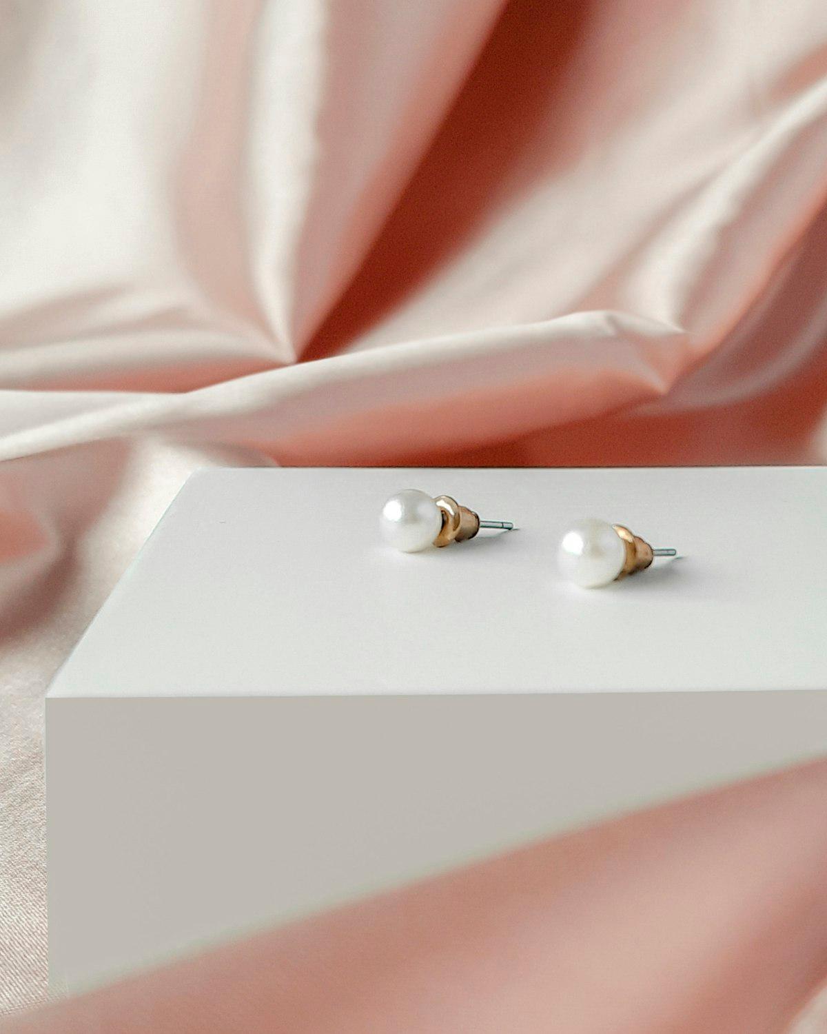 Par de zarcillos de perla sobre un bloque blanco con tela rosa