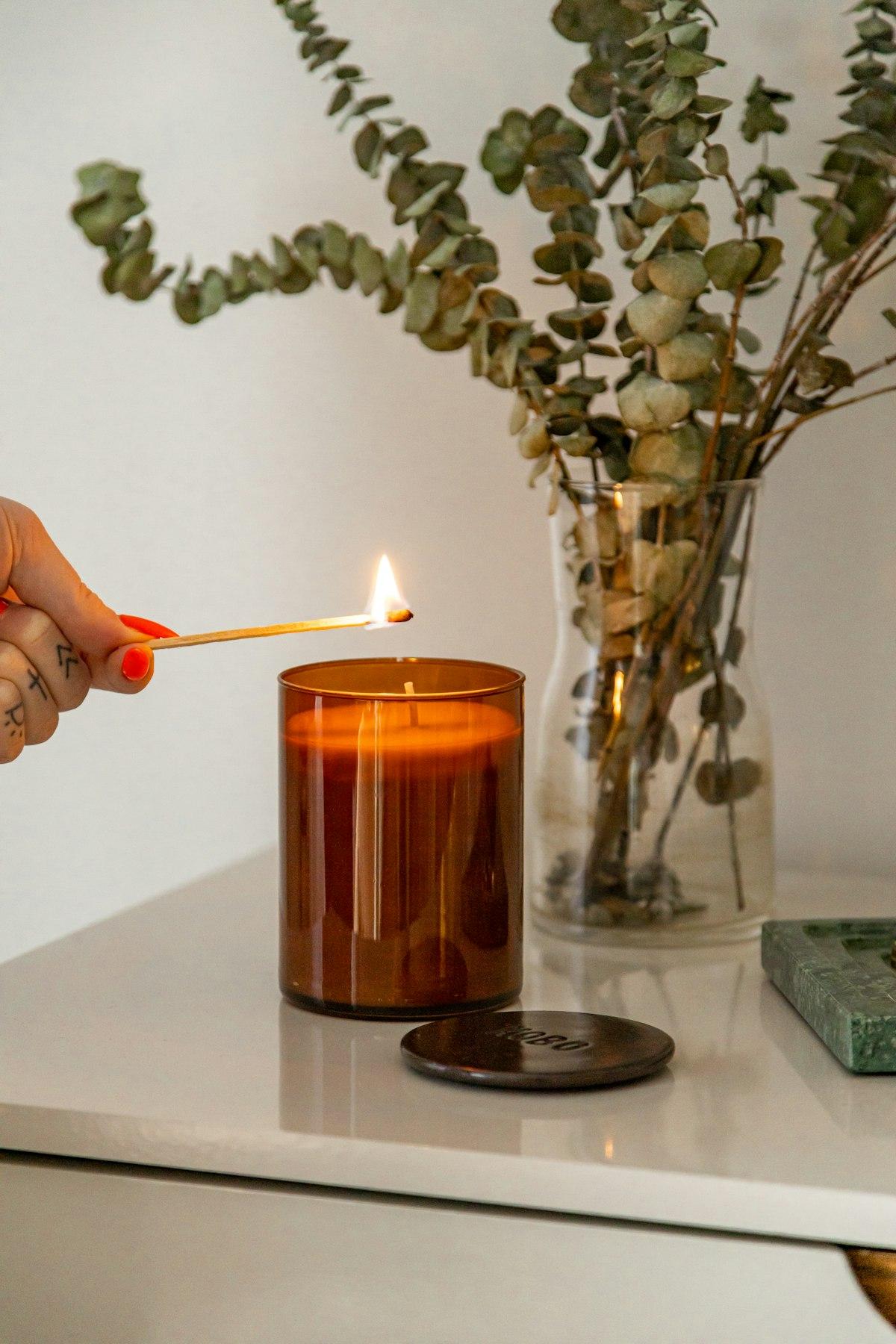 Mano encendiendo una vela en frasco de vidrio ámbar