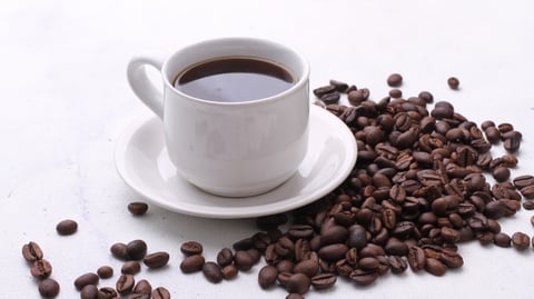 A cup of coffee with coffee beans, as the American Heart Association says up to five daily cups may lower heart disease risk