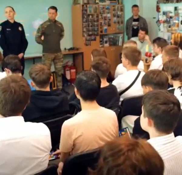 Law enforcement officers in uniform address a classroom of teenagers during a security awareness briefing on online recruitment and sabotage