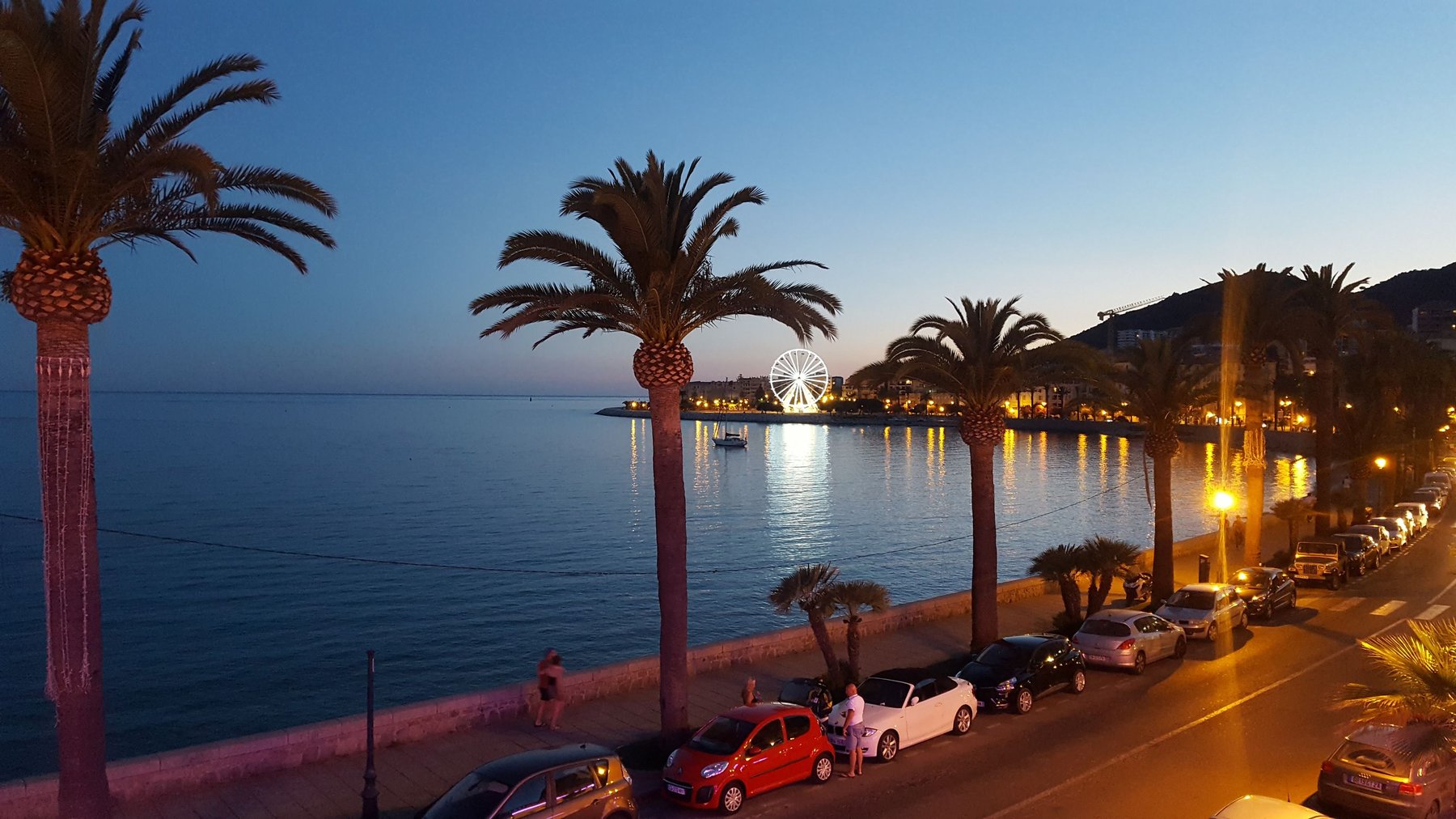 A road lit by street lights with a view of the sea.