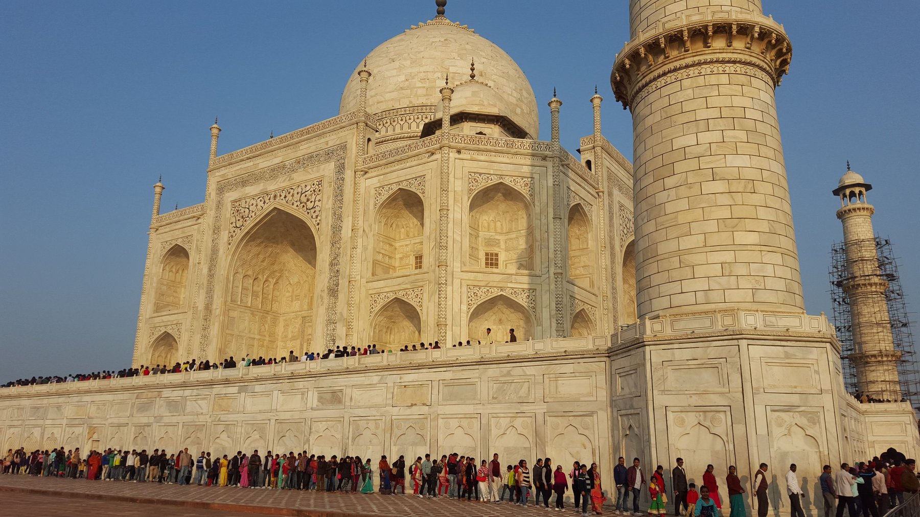Many people queue around a grand, white marble mausoleum.