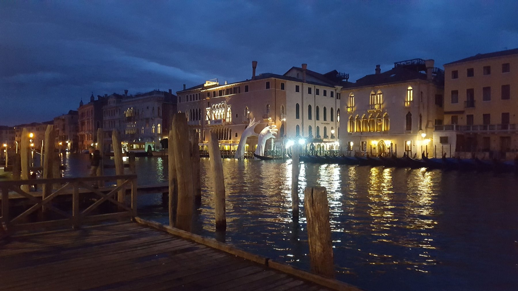 A canal at night with giant stone hands protruding from the water.