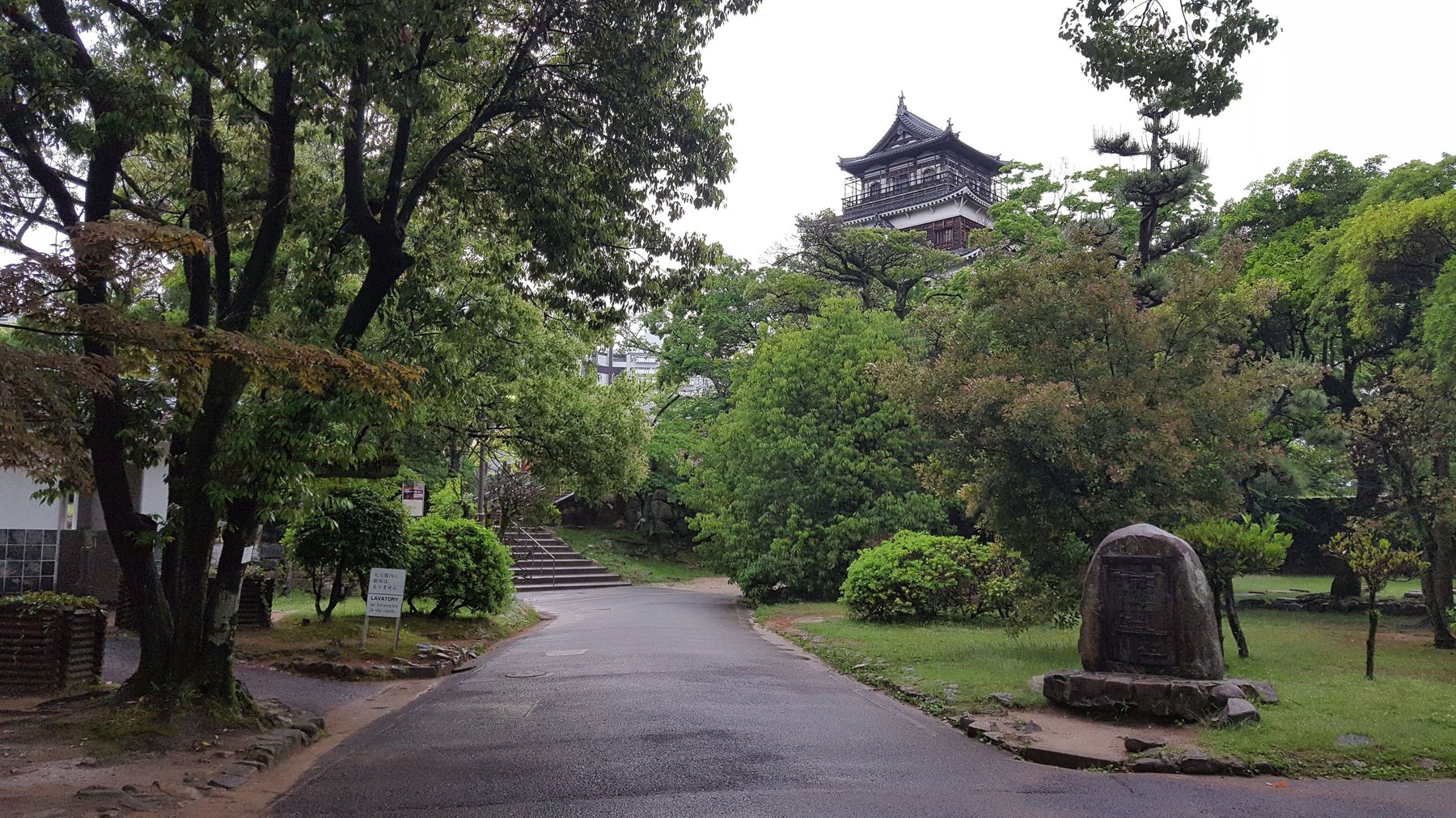 A Japanese castle can be seen towering above trees in a leafy garden.