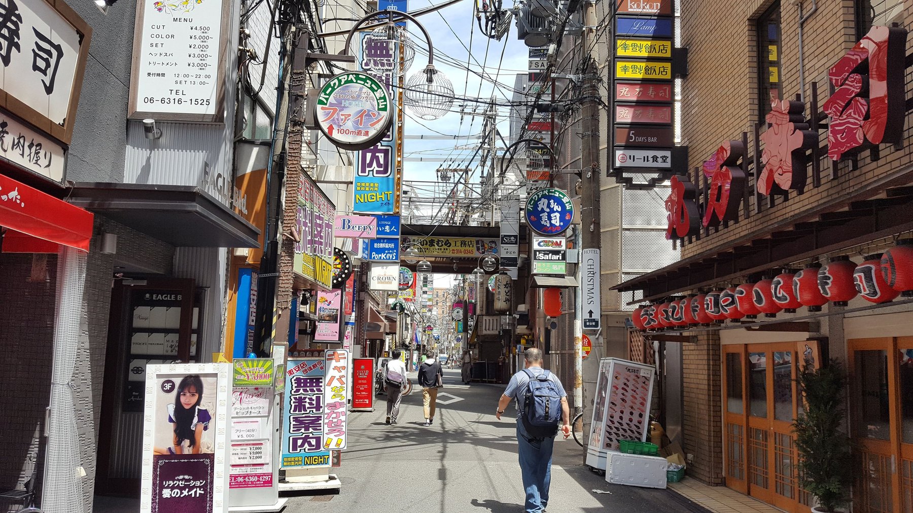 A small street in the daytime, cluttered with lamps, shopfronts and signs.