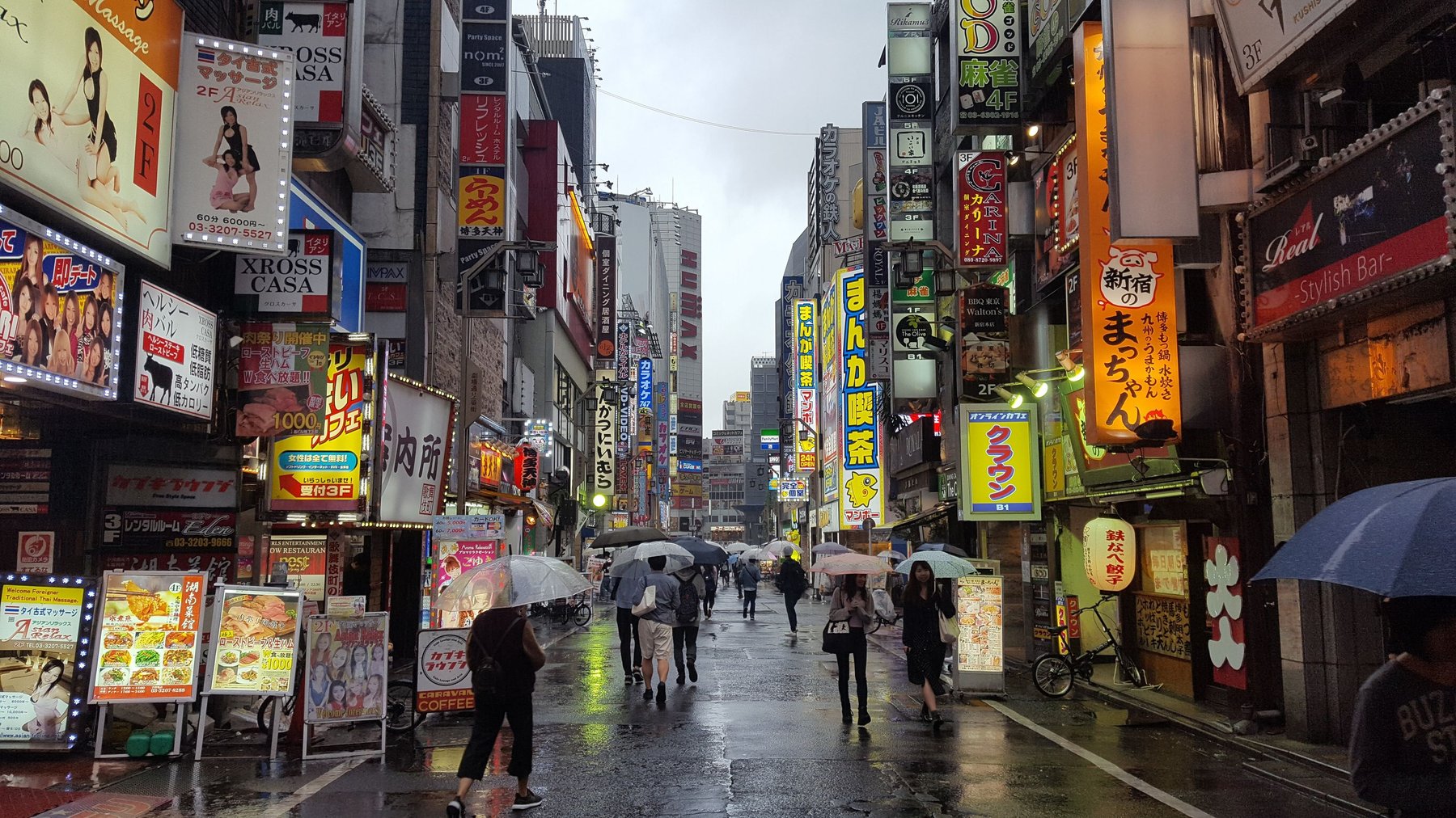 People walking in the rain with umbrellas under bright Japanese shop signs.