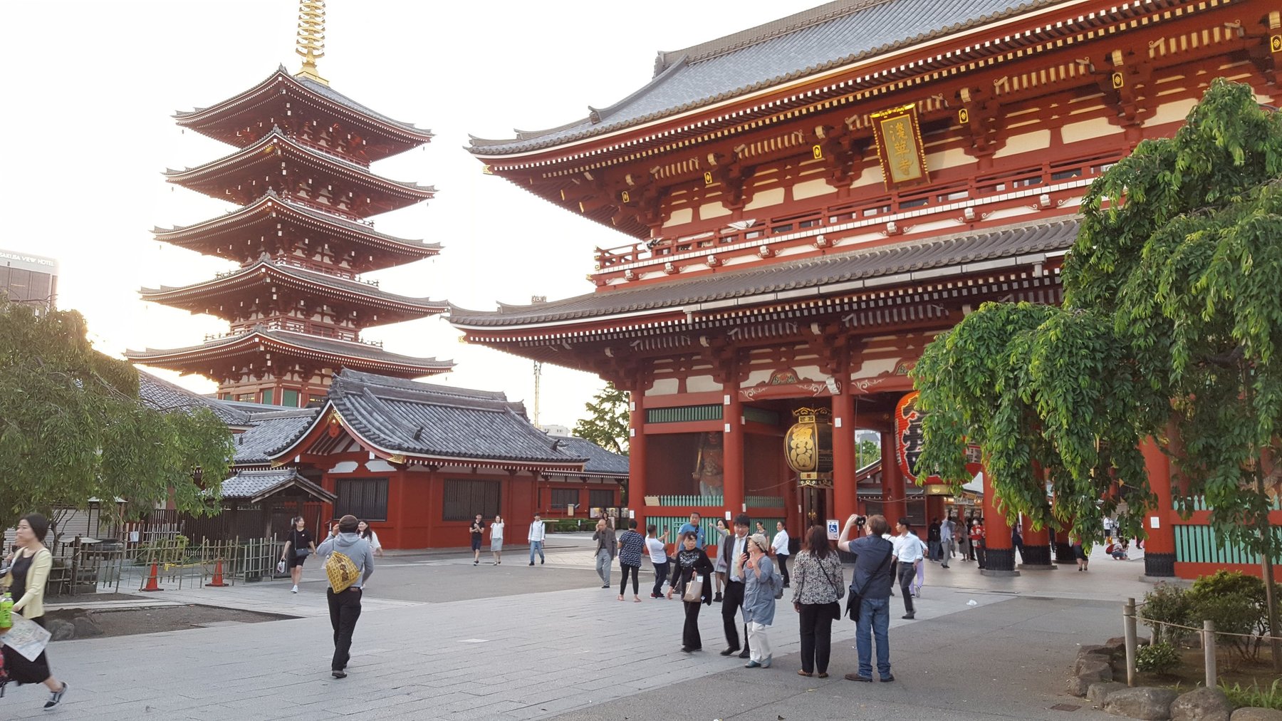 An ornate Japanese temple gate stands to the right of a five-storied tower with distinctive roofs on each floor.
