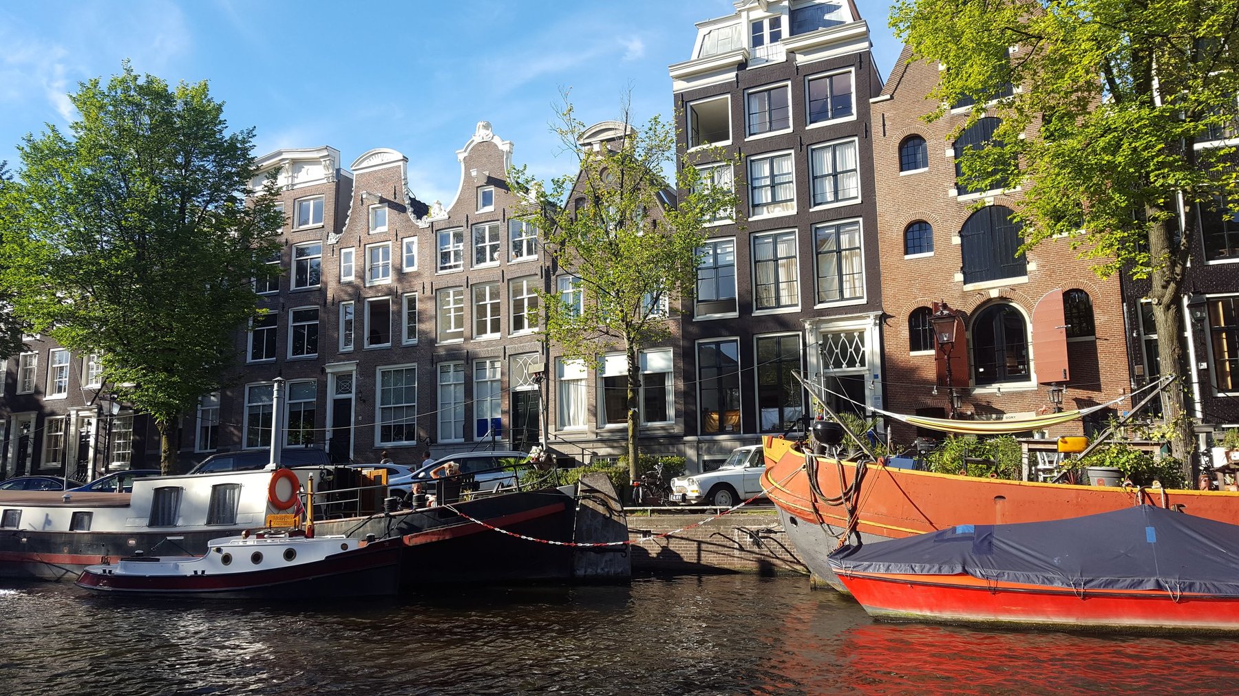 Grand houses in front of a canal with colourful boats docked in front.
