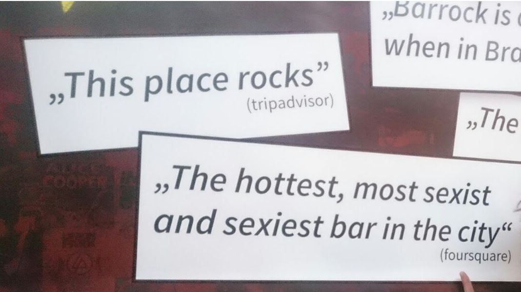 A sign outside a bar displays reviews, reading “This place rocks (tripadvisor)” and “The hottest, most sexist and sexiest bar in the city (foursquare)”.